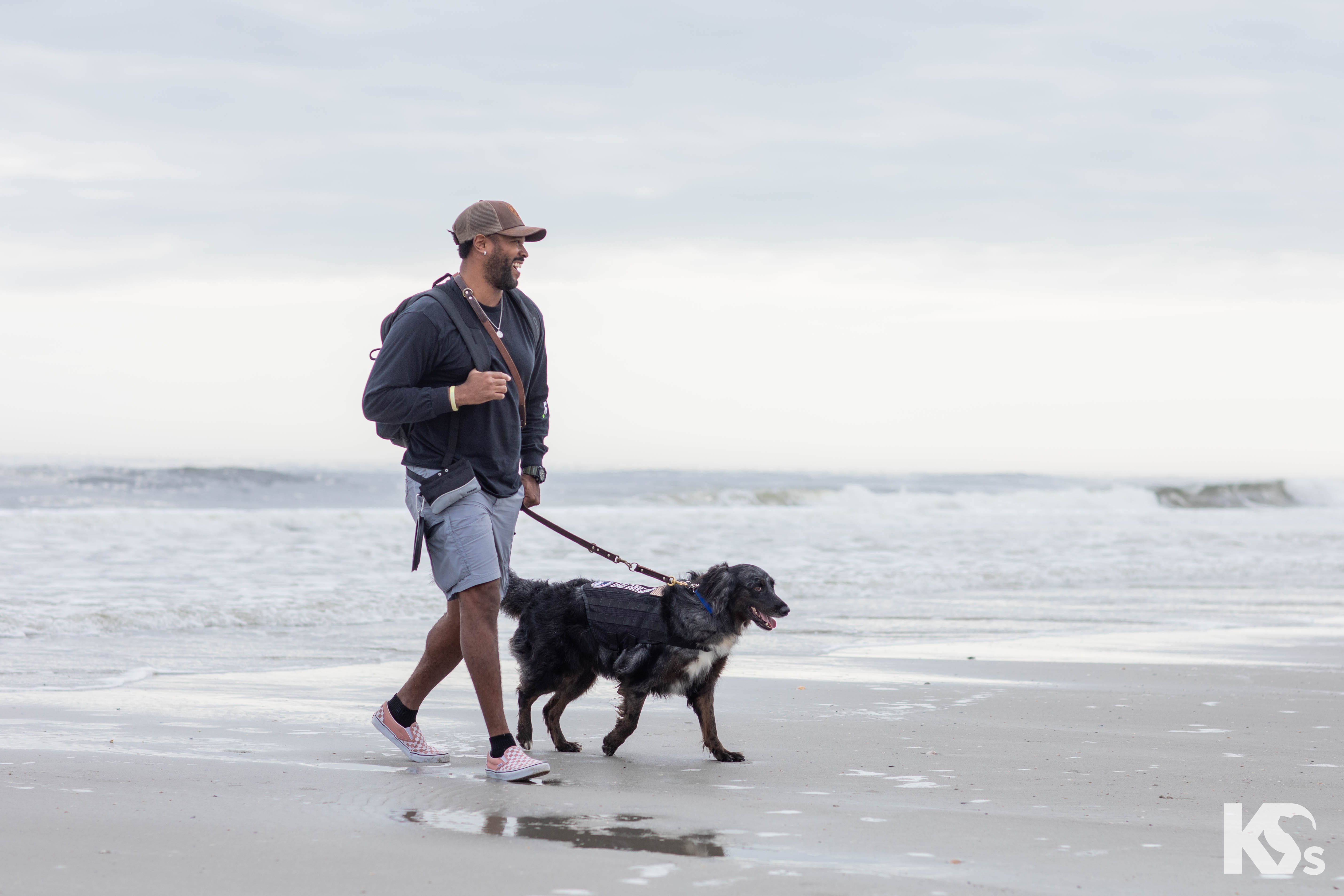 Veteran service dog and man walking along a beach.
