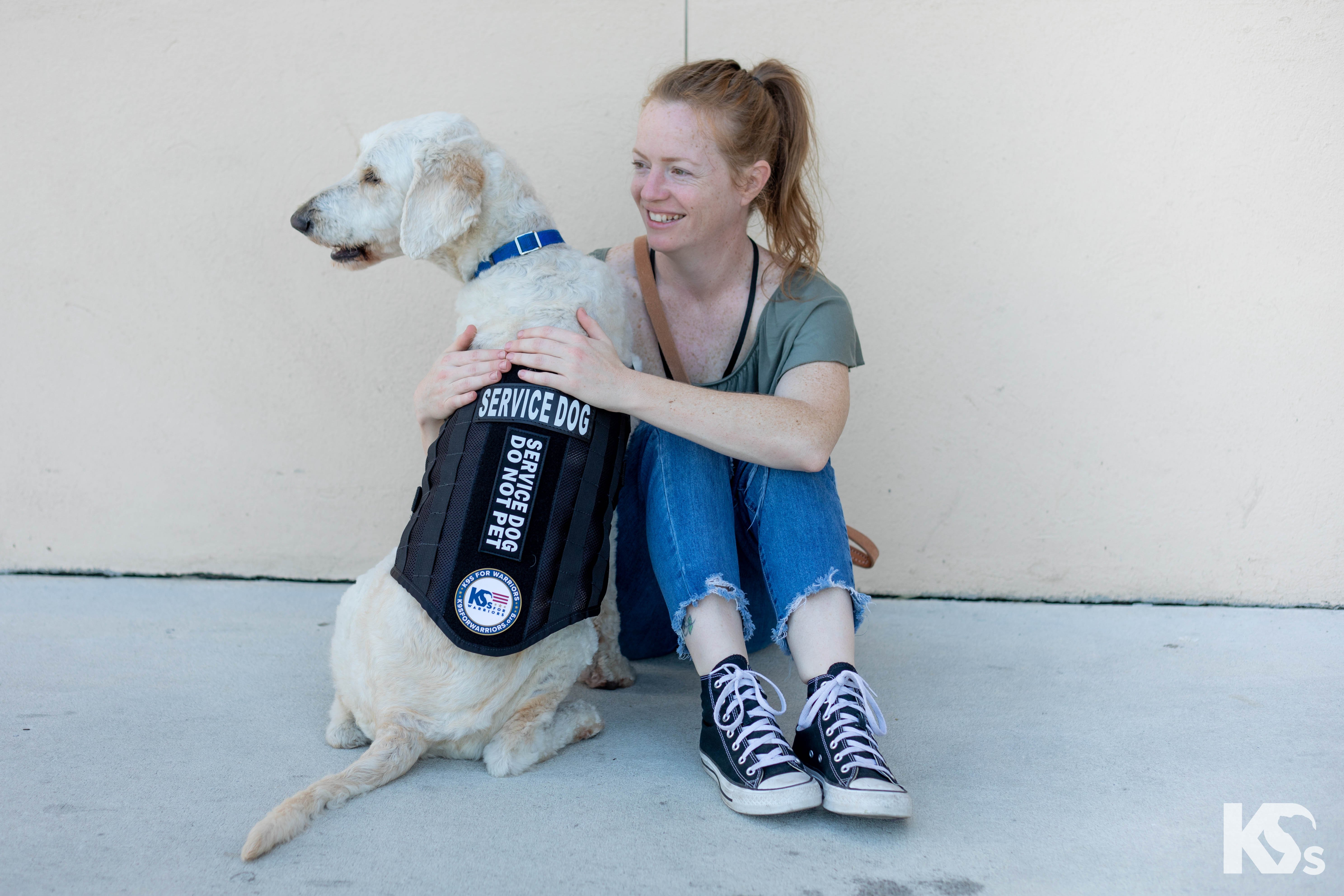 Woman and veteran service dog sitting on the ground.